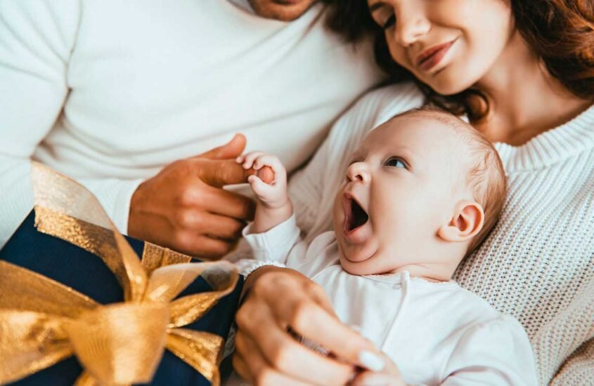 Bébé heureux sur les genoux de ses parents avec un cadeau à ses côtés